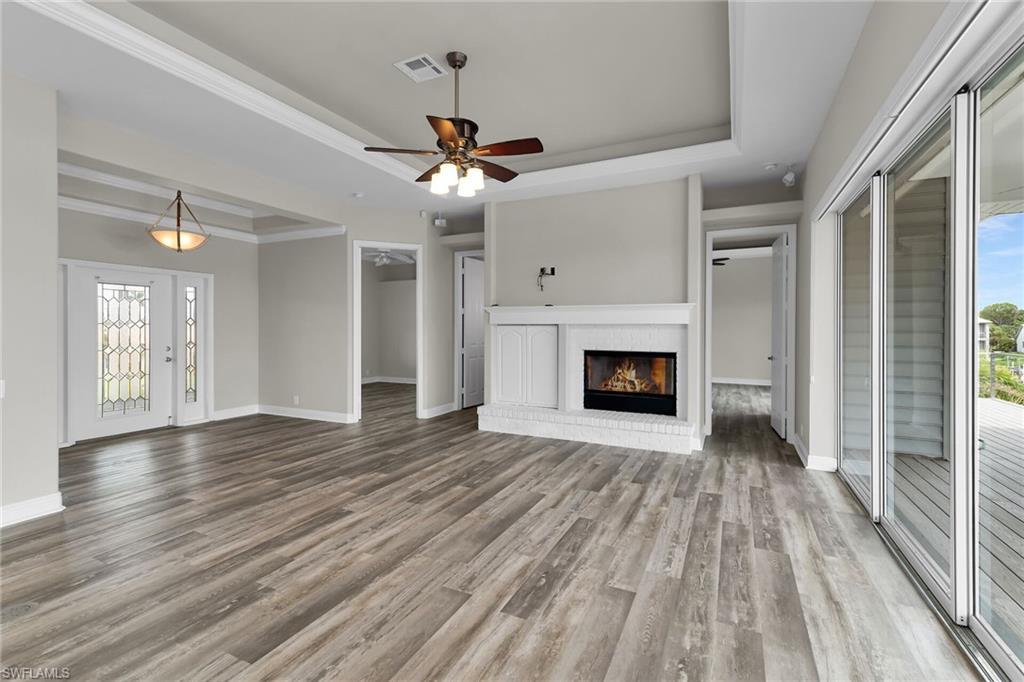 Image 3: Unfurnished living room featuring a raised ceiling, wood finished floors, a brick fireplace, ceiling fan, and ornamental molding