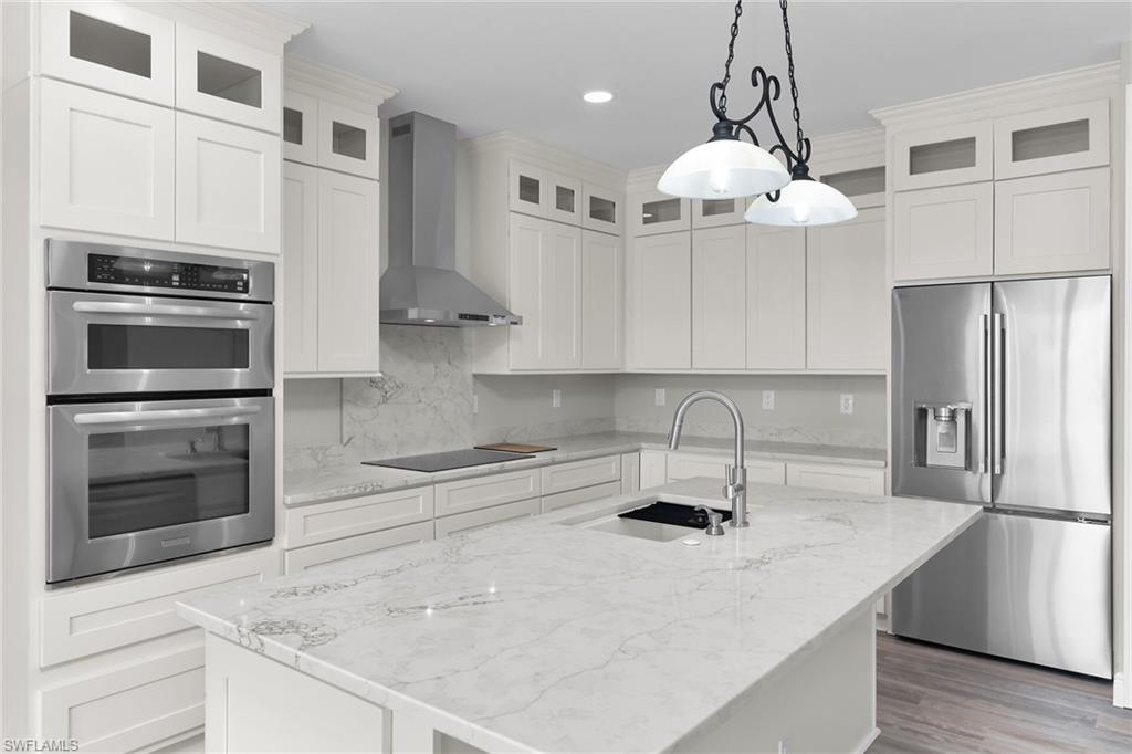 Image 4: Kitchen with appliances with stainless steel finishes, wall chimney exhaust hood, an island with sink, pendant lighting, and recessed lighting