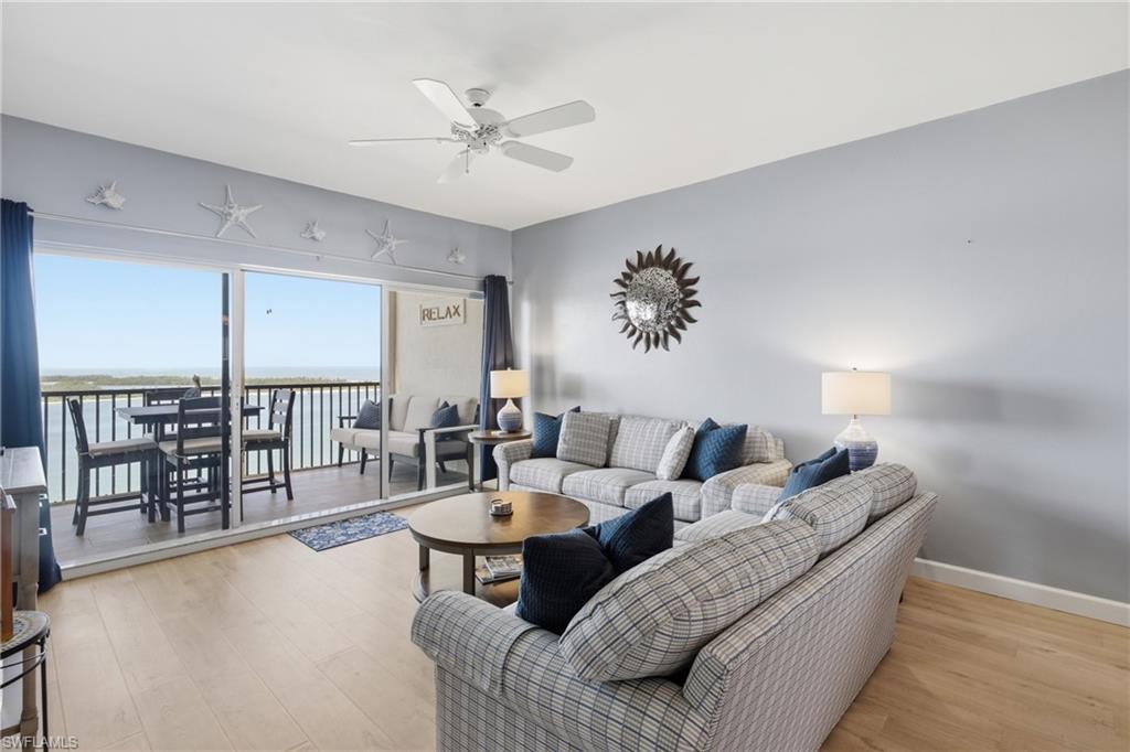 Image 4: Spacious living area featuring light wood-finish flooring, a ceiling fan, and direct access to a private balcony through a large sliding glass door - Virtually Edited Image