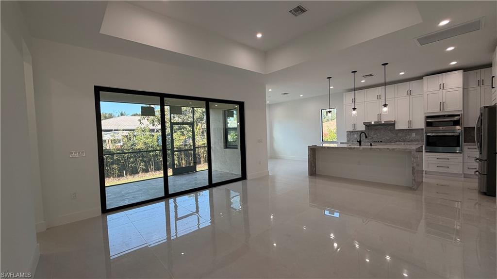 Image 2: Kitchen with light stone counters, a kitchen island with sink, appliances with stainless steel finishes, pendant lighting, and white cabinetry