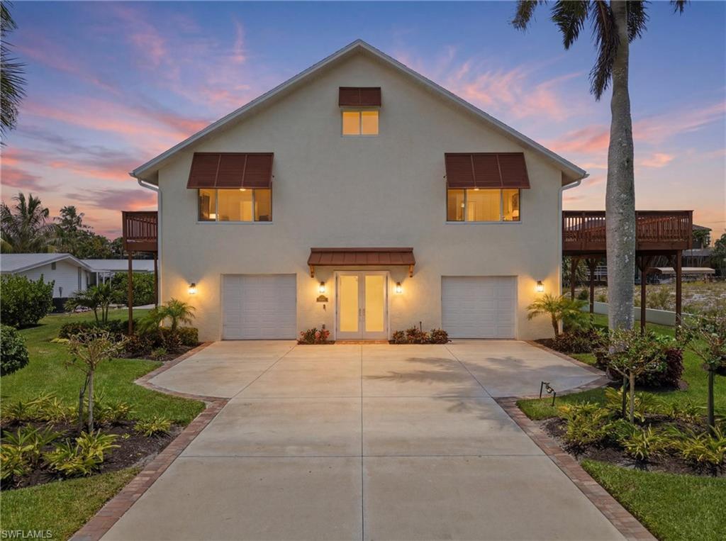 Image 1: Two-story stucco home featuring a central entry with transom window, two integrated garages, and two elevated wood decks