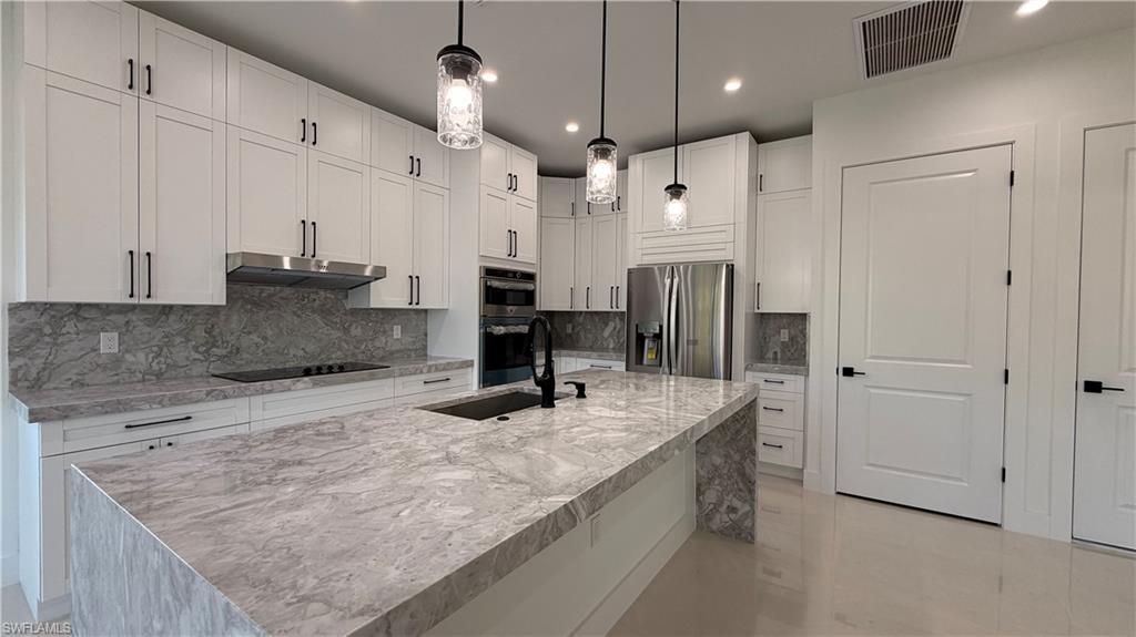 Image 4: Kitchen featuring appliances with stainless steel finishes, recessed lighting, light stone countertops, white cabinetry, and a center island with sink