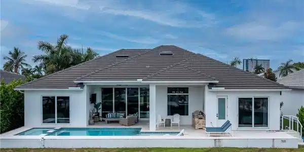 Image 4: Modern architectural residence featuring a clean-lined white exterior with charcoal tile roofing, expansive glass sliding doors and windows, and a resort-style backyard with heated swimming pool, mature tropical landscaping including palm trees, manicured lawn, and integrated hardscape patio areas ideal for outdoor entertaining