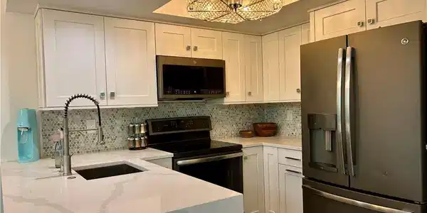 Image 3: Modern kitchen featuring white shaker cabinetry, patterned tile backsplash, and quartz countertops with integrated sink