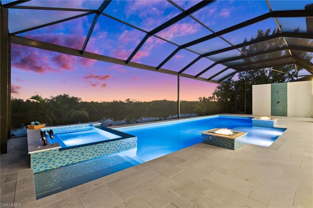Image 3: Pool at dusk with a fire pit, a lanai, a patio area, pool water feature, and an in ground hot tub