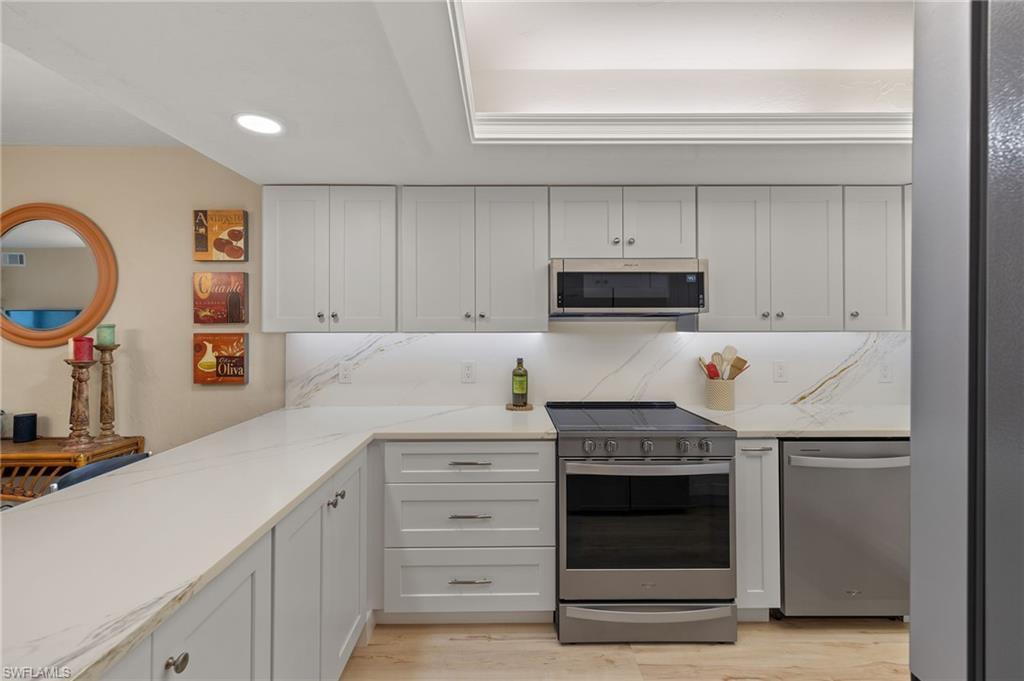 Image 2: Kitchen with white cabinets, decorative backsplash, light hardwood / wood-style floors, light stone counters, and stainless steel appliances