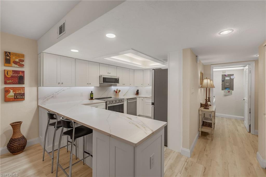 Image 3: Kitchen with kitchen peninsula, appliances with stainless steel finishes, a breakfast bar, light hardwood / wood-style floors, and white cabinetry