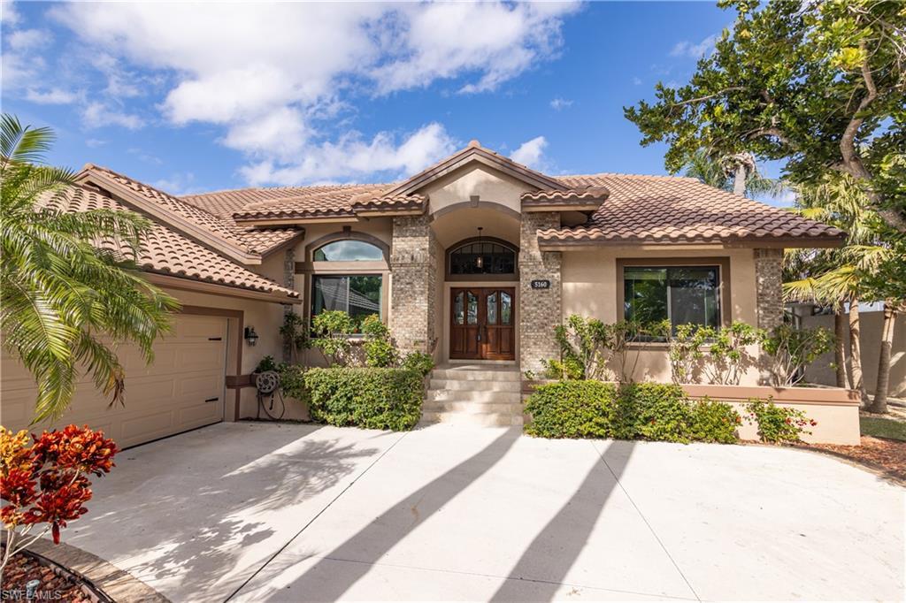 Image 2: Mediterranean-style residence featuring a tile roof, stucco exterior, stone accents, and a double wood-finish entry door with an arched transom