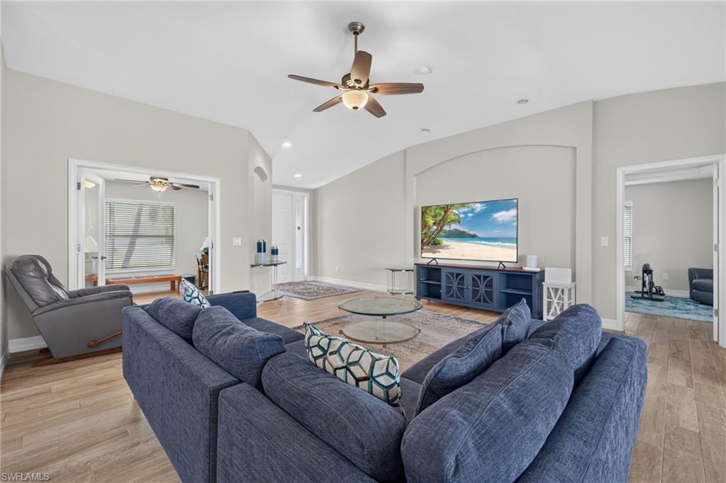Image 3: Spacious living area featuring light wood-finish flooring, vaulted ceilings, recessed lighting, and a ceiling fan