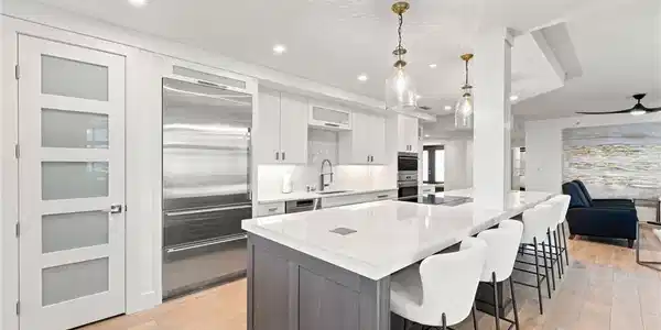 Image 2: Gourmet kitchen featuring a large island, integrated stainless steel refrigerator, recessed lighting, white cabinetry, and wood-finish flooring