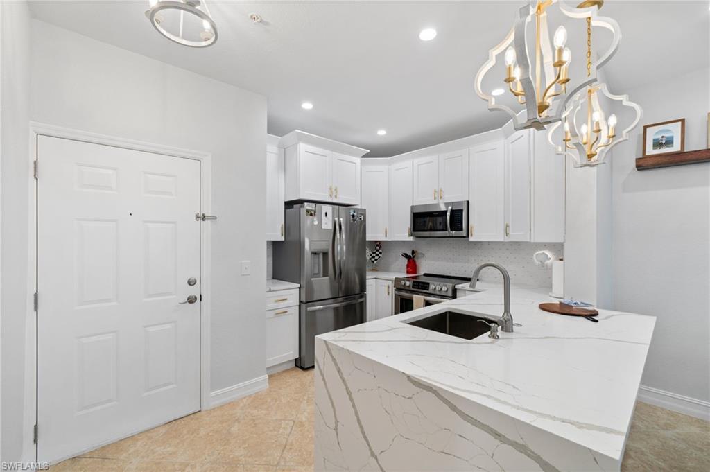 Image 4: Kitchen featuring light stone countertops, a peninsula, white cabinets, stainless steel appliances, and a chandelier