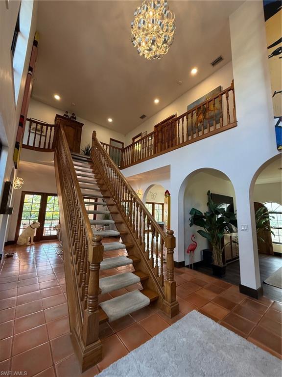 Image 4: Staircase featuring a towering ceiling, a chandelier, arched walkways, recessed lighting, and tile patterned floors