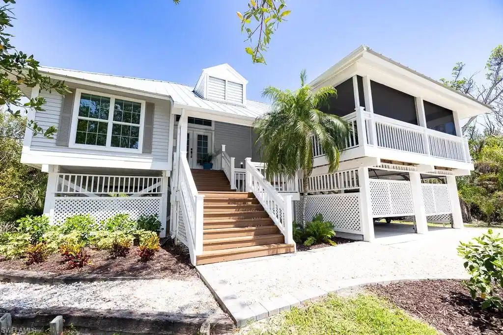 Image 1: Elevated coastal-style residence featuring a metal roof, screened porch, wood-finish exterior stairs, lattice foundation skirting, and gravel driveway