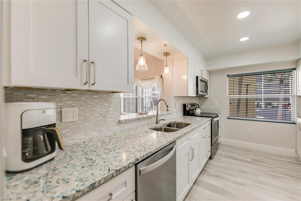 Image 3: Kitchen featuring appliances with stainless steel finishes, decorative backsplash, white cabinetry, recessed lighting, and light stone counters