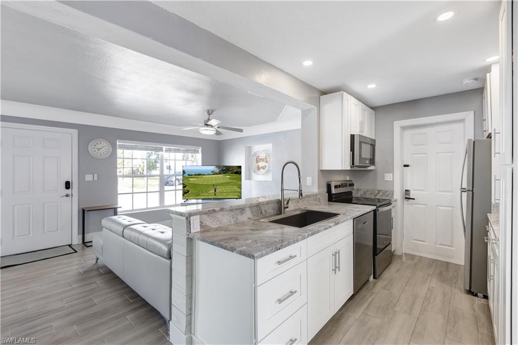 Image 2: Modern kitchen featuring white cabinetry, stone countertops, stainless steel appliances, and a built-in sink with a gooseneck faucet
