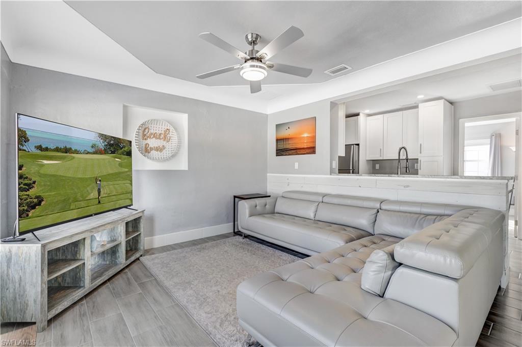 Image 4: Open-concept living space featuring wood-finish tile flooring, a recessed ceiling with a ceiling fan, and a kitchen pass-through with a built-in counter