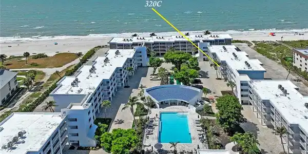 Image 2: Island Beach Club 320C features a beachfront location with direct oceanfront access, a resort-style heated swimming pool surrounded by mature landscaping, contemporary multi-story residential architecture with clean lines and white exterior finishes, and expansive grounds with hardscaped amenities and green space