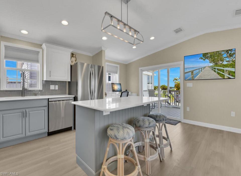Image 4: Kitchen with light wood-type flooring, appliances with stainless steel finishes, lofted ceiling, backsplash, and decorative light fixtures