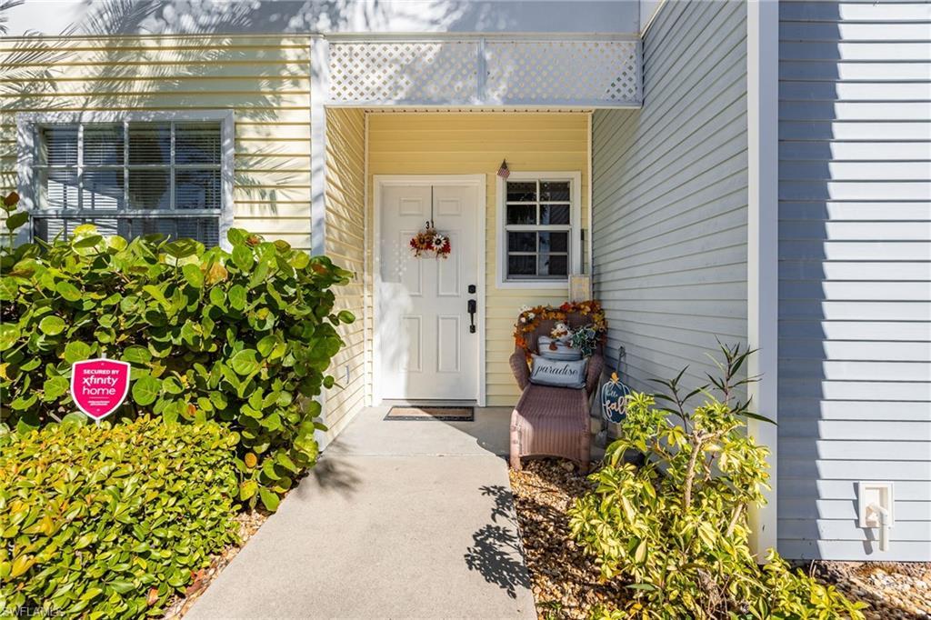Image 2: Entryway featuring a white door, yellow horizontal siding, a white lattice overhang, a window with white trim, and a concrete pathway