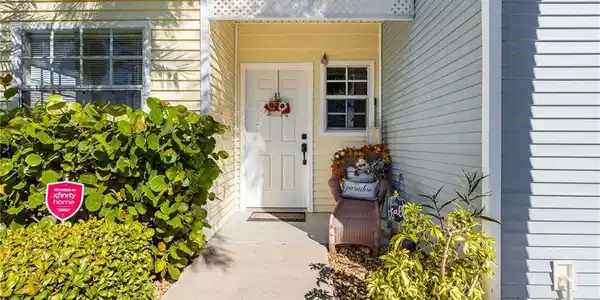 Image 2: Entryway featuring a white door, yellow horizontal siding, a white lattice overhang, a window with white trim, and a concrete pathway