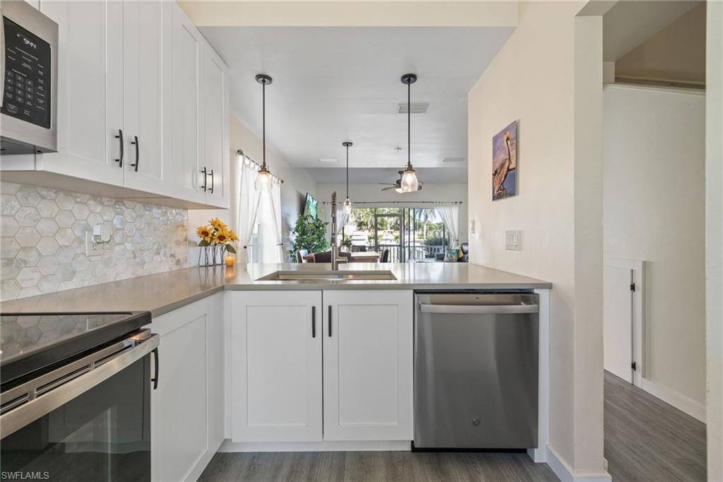 Image 4: Kitchen featuring white shaker-style cabinetry, stainless steel appliances, a hexagonal tile backsplash, and light-toned countertops