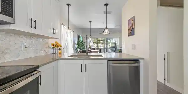Image 4: Kitchen featuring white shaker-style cabinetry, stainless steel appliances, a hexagonal tile backsplash, and light-toned countertops