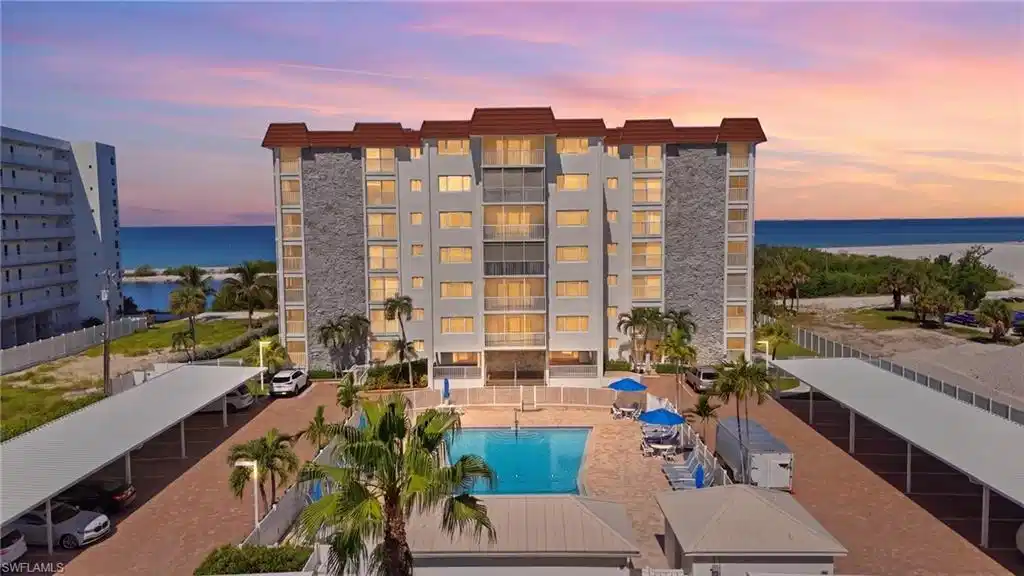 Image 1: Multi-story building featuring balconies, beachfront access, a swimming pool, and covered parking - Virtually Edited Image