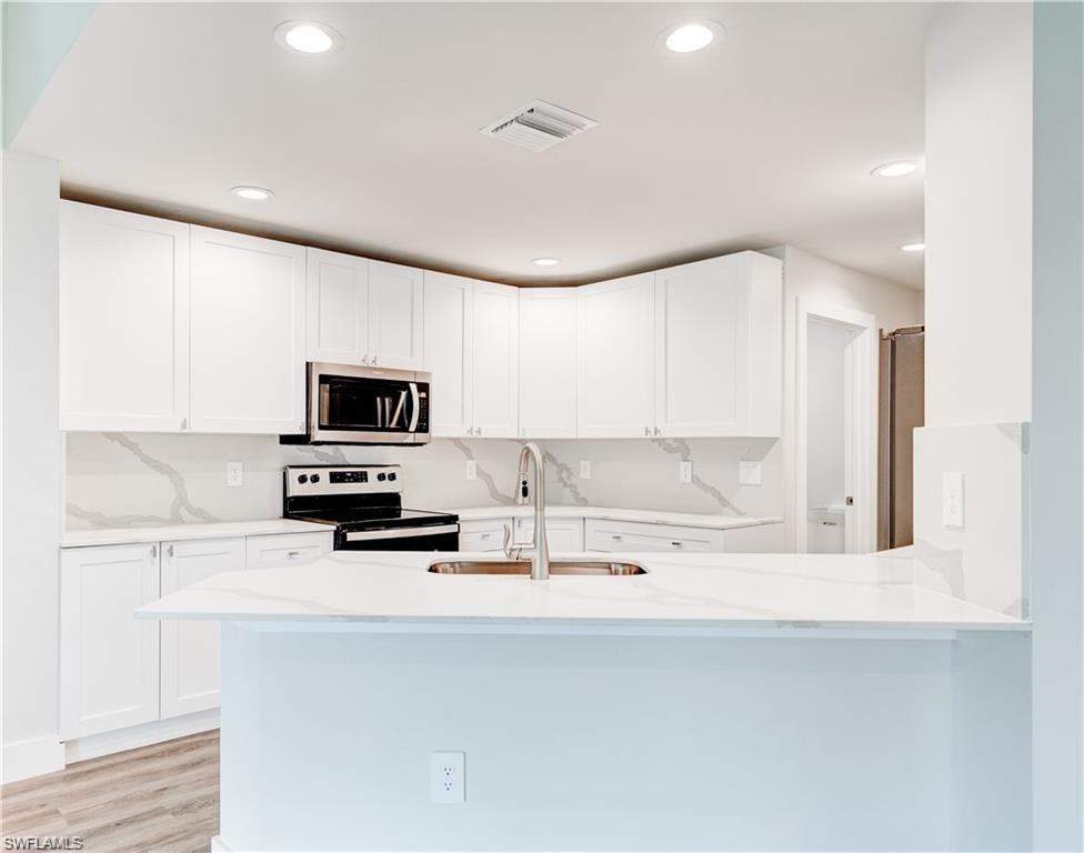Image 3: Kitchen featuring stainless steel appliances, white cabinets, light stone counters, a peninsula, and recessed lighting