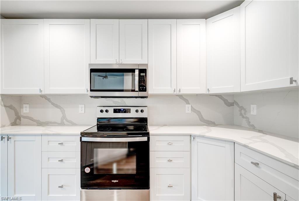 Image 4: Kitchen with stainless steel appliances, white cabinetry, and light stone counters