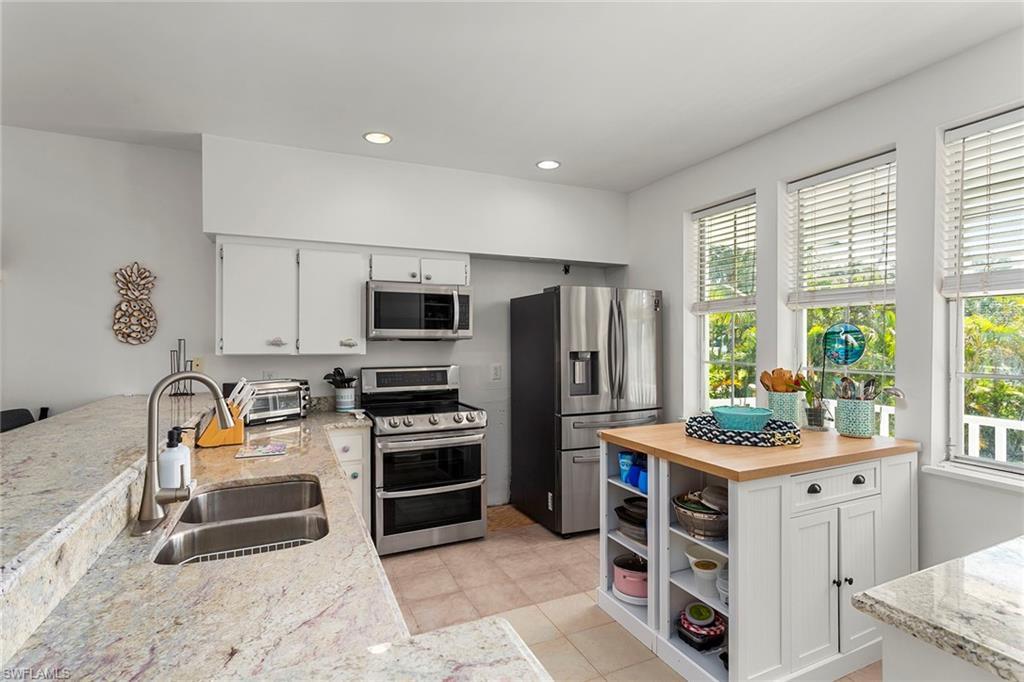 Image 3: Kitchen featuring white cabinetry, open shelves, stainless steel appliances, light stone countertops, and recessed lighting