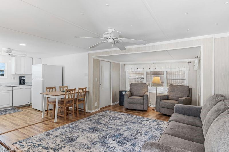 Image 4: Open-concept living area featuring wood-finish laminate flooring, a ceiling fan, and white cabinetry in the kitchen space.