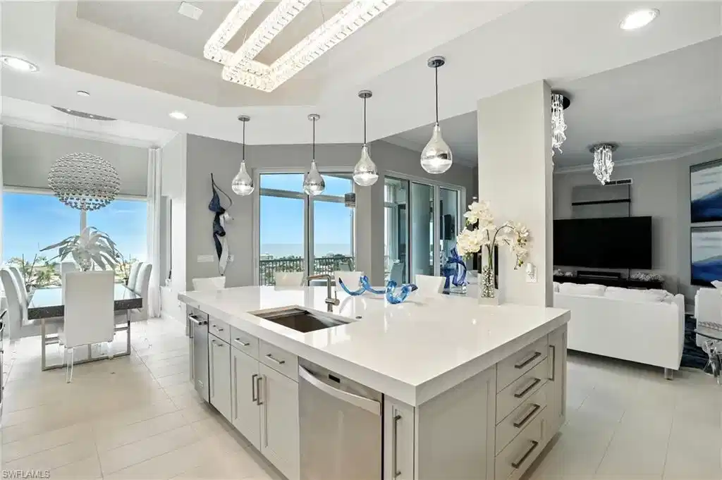 Image 1: Kitchen featuring crown molding, a chandelier, a tray ceiling, pendant lighting, and stainless steel dishwasher - Virtually Edited Image