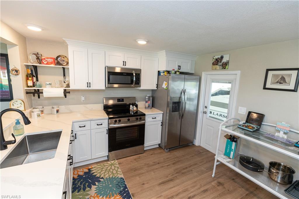 Image 2: Kitchen featuring white cabinetry with dark hardware, a stainless steel appliance suite, white countertops, wood-finish flooring, and recessed lighting
