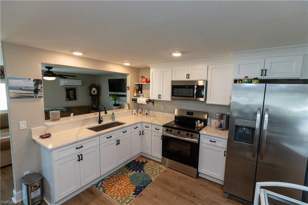 Image 3: Kitchen featuring white shaker-style cabinetry, stainless steel appliances, a built-in microwave, wood-finish flooring, and light-toned countertops