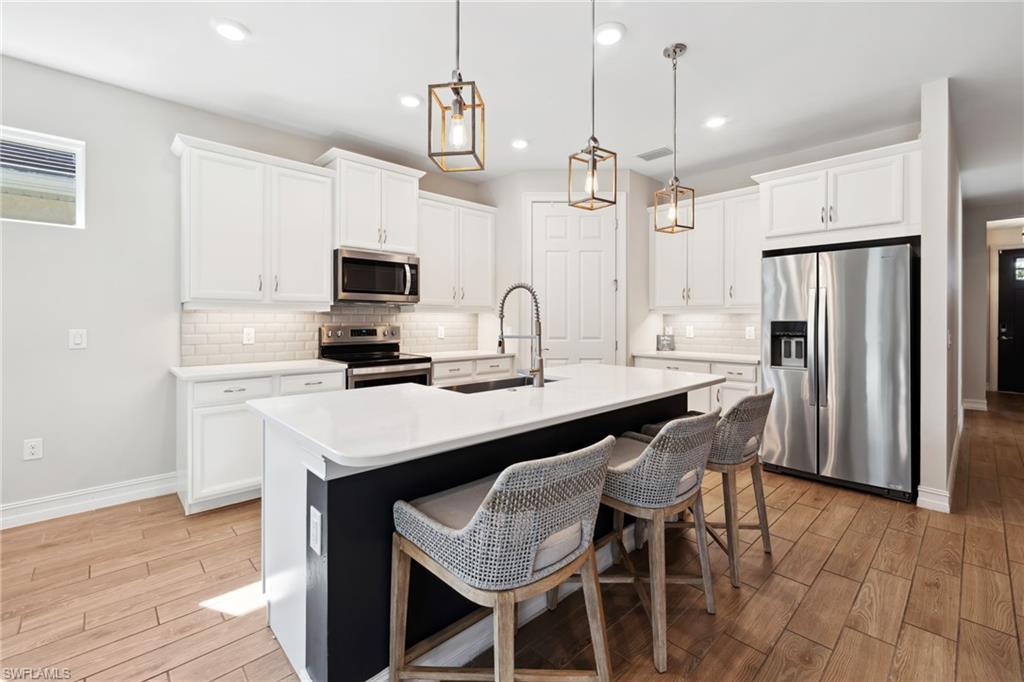 Image 4: Kitchen with wood tiled floors, appliances with stainless steel finishes, white cabinets, a kitchen breakfast bar, and recessed lighting