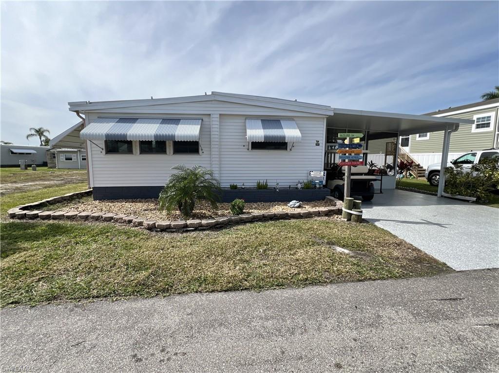 Image 1: Manufactured / mobile home featuring a carport, concrete driveway, a front yard, and enclosed/covered lanai.
