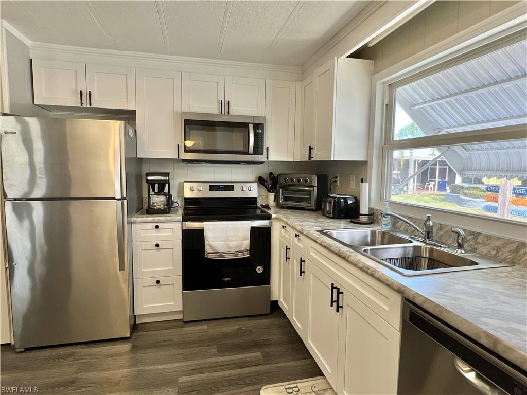 Image 4: Kitchen featuring stainless steel appliances, white cabinets, light countertops, and dark wood-style vinyl floors