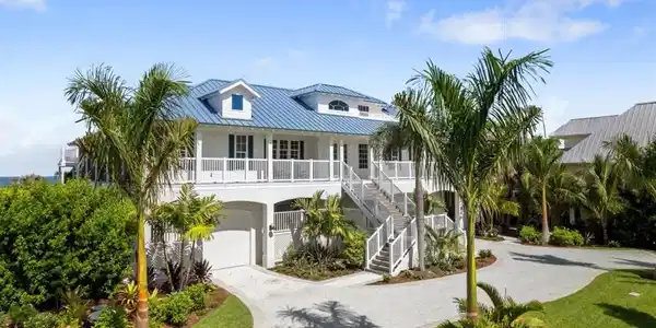 Image 2: Coastal inspired home featuring gravel driveway, a metal roof, stairs, an attached garage, and stucco siding