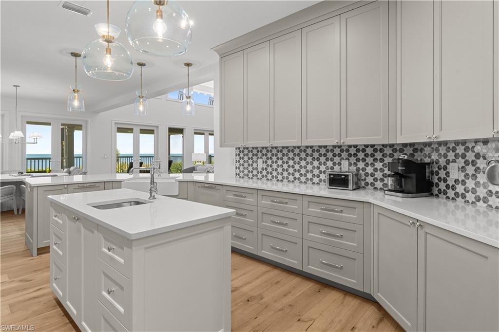 Image 4: Kitchen with decorative light fixtures, backsplash, a peninsula, light stone countertops, and light wood finished floors