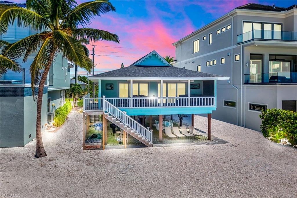 Image 2: Back of house at dusk with stairs, a shingled roof, stucco siding, and a balcony