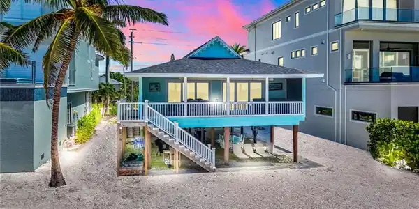 Image 2: Back of house at dusk with stairs, a shingled roof, stucco siding, and a balcony