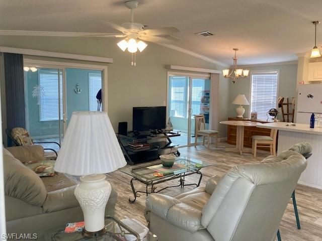 Image 4: Living room with ornamental molding, vaulted ceiling, a ceiling fan, light wood finished floors, and a chandelier
