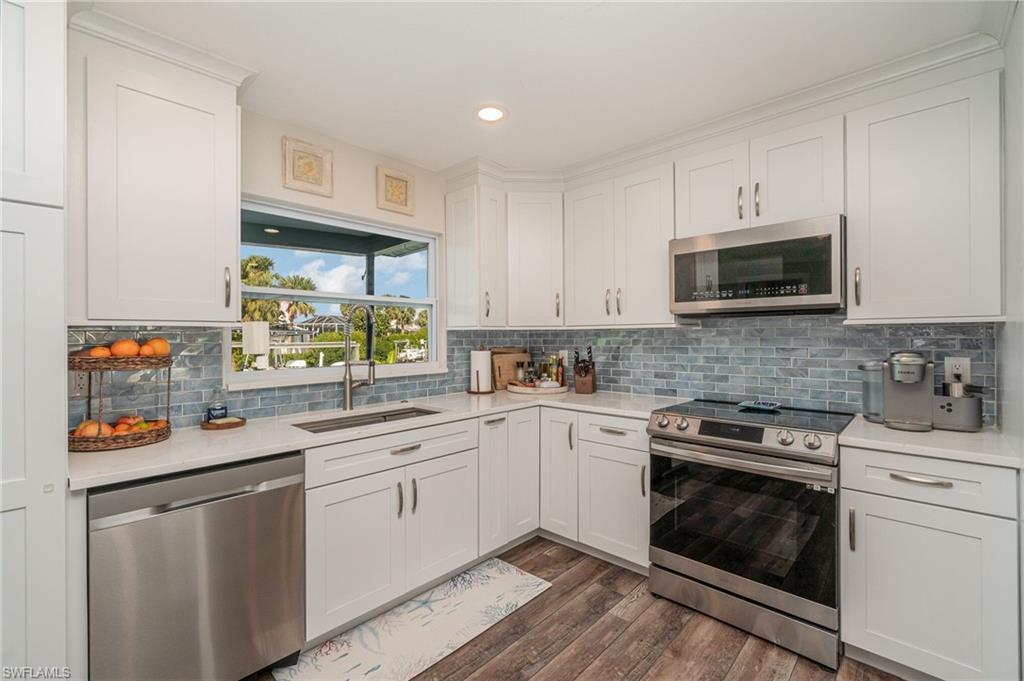 Image 4: Kitchen with stainless steel appliances, white cabinets, dark wood finished floors, backsplash, and recessed lighting