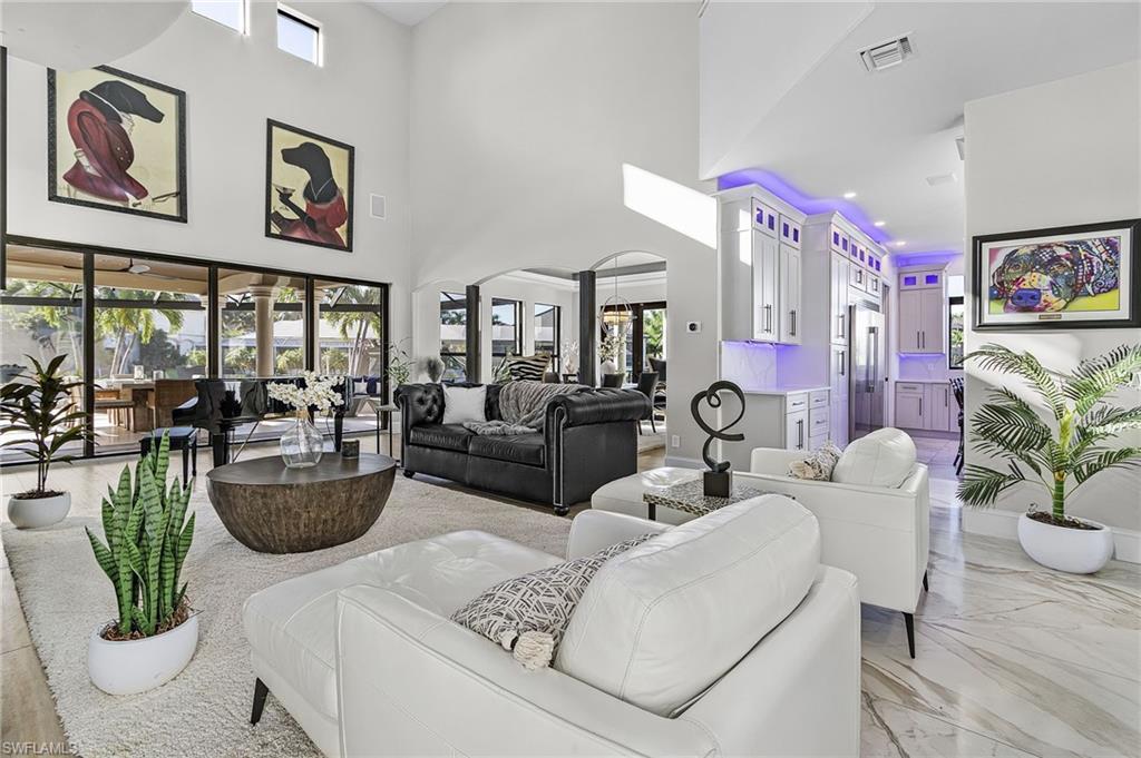 Image 3: Living room with grand piano,  arched walkways, a fireplace, light wood-style floors, and a high ceiling