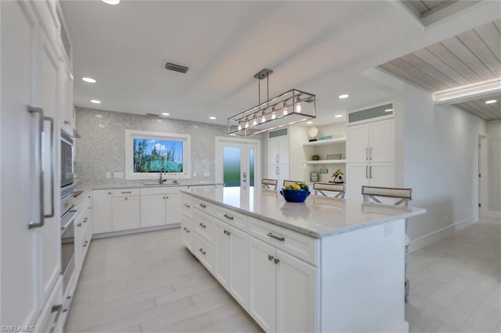 Image 4: Kitchen with white cabinets, a breakfast bar, light stone counters, a kitchen island, and decorative light fixtures