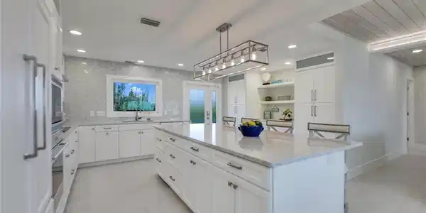 Image 4: Kitchen with white cabinets, a breakfast bar, light stone counters, a kitchen island, and decorative light fixtures
