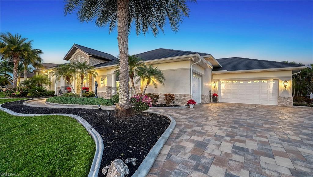 Image 3: View of front facade featuring stone siding, a garage, decorative driveway, stucco siding, and a lawn