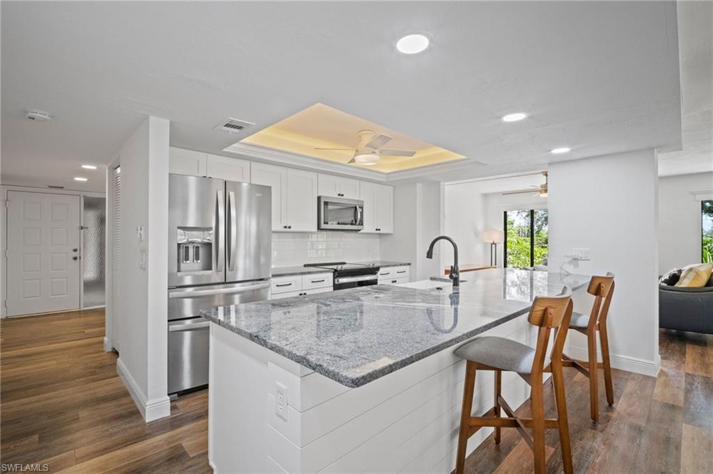 Image 3: Kitchen featuring a tray ceiling, light stone counters, stainless steel appliances, white cabinetry, and recessed lighting