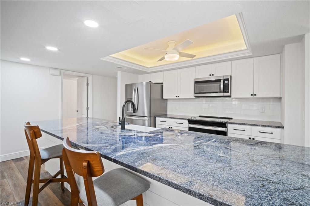 Image 4: Kitchen with a tray ceiling, backsplash, wood finished floors, white cabinetry, and recessed lighting