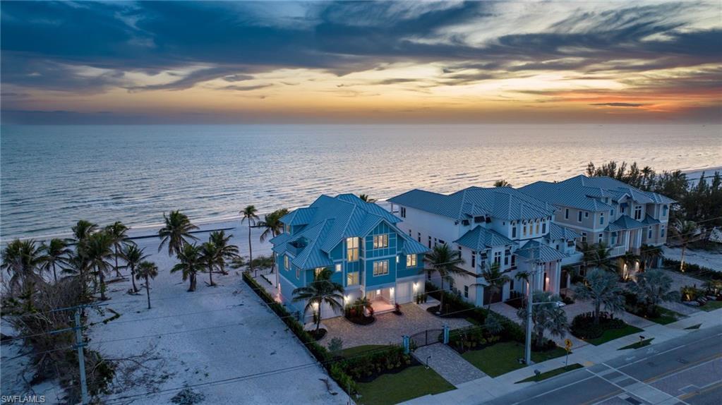 Image 2: Breathtaking Gulf-Front Estate at Sunset - the warm glow of the home contrasts beautifully with the serene Gulf waters and dramatic sunset skies- Photo Virtually Edited